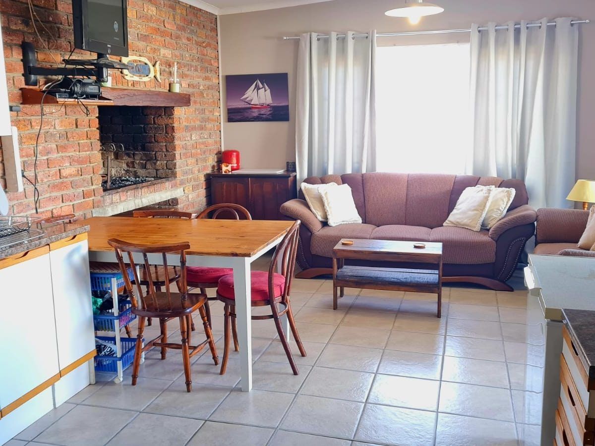 Open-plan lounge at Galjoen Gat with brick indoor braai, dining table, couches, and sailing-themed artwork