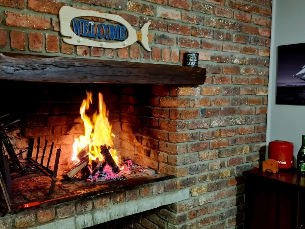 Brick indoor braai at Galjoen Gat with a wood fire burning and a fish-themed welcome sign above