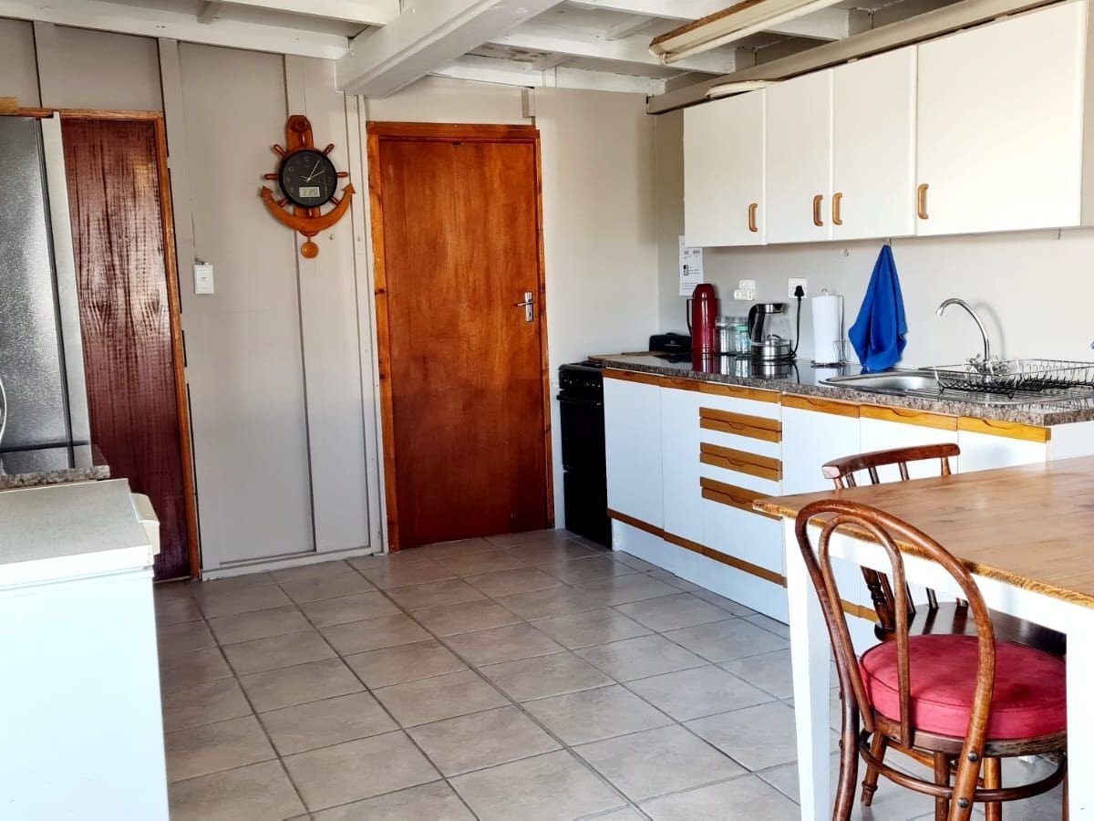 Kitchen at Galjoen Gat with a ship-wheel wall clock, white cabinets, stove, fridge, and dining table