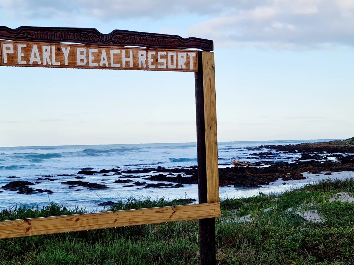 Wooden Pearly Beach Resort entrance sign with the rocky shoreline and ocean visible behind